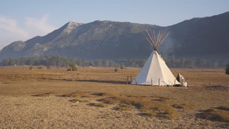 Tepee-tipi-tent-in-middle-of-dry-vast-field,-establisher-shot,-pan-reveals-landscape