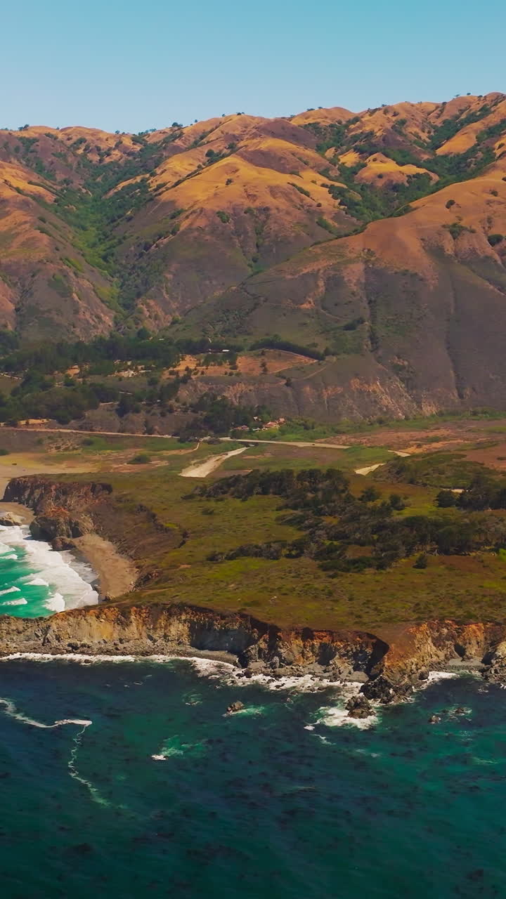 Amazingly beautiful shades of blue in the ocean near rocky shore. Brown orange mountains with rounded tops at backdrop. Vertical video