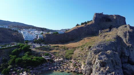 Agios-Pavlos-beach-in-Rhodes,-Greece-with-Acropolis-of-Lindos,-houses-and-Mediterranean-sea-during-the-day-filmed-with-the-drone