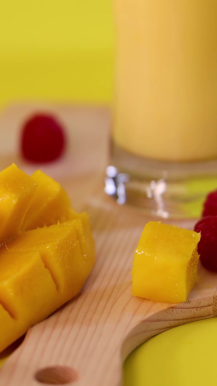 Cubetti di mango fresco e frullato disposti su un tagliere con lamponi, fiori e illuminazione vivida