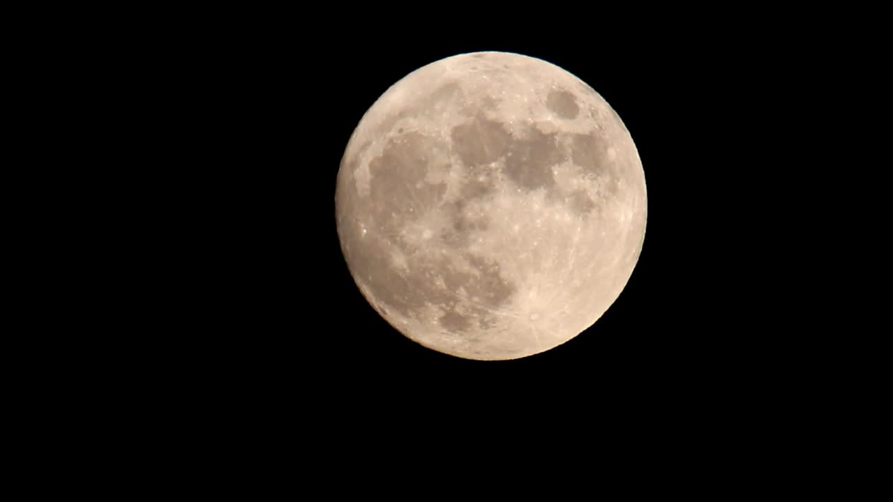 Lua cheia laranja e amarela brilhante contra um céu preto escuro, movendo-se do centro do quadro ligeiramente para o canto superior direito