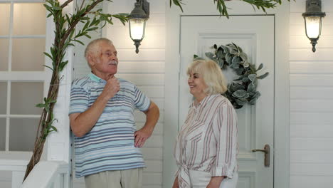 senior couple together in porch at home. mature man stands and his wife comes to embrace him