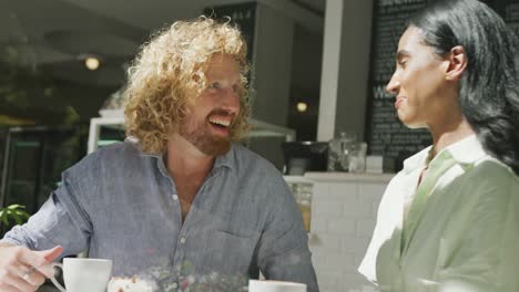 happy diverse couple drinking coffee and talking in cafe