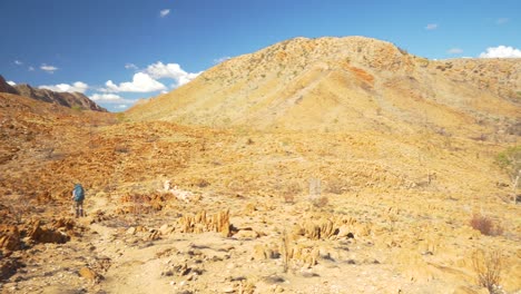 Pan-past-hiker-across-mountainous-desert-landscape,-Central-Australia