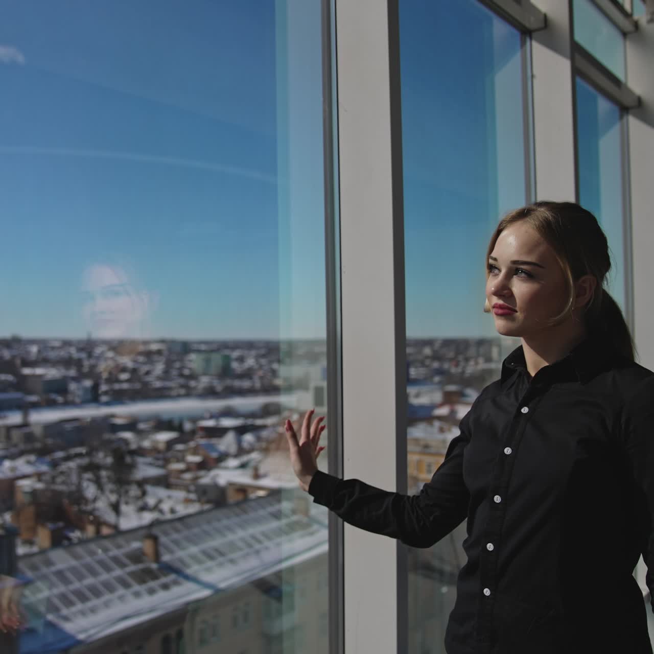 Attractive female enjoying the sunrays coming through the big panoramic window. Great look at the city from the office center. Close up with gradual distancing