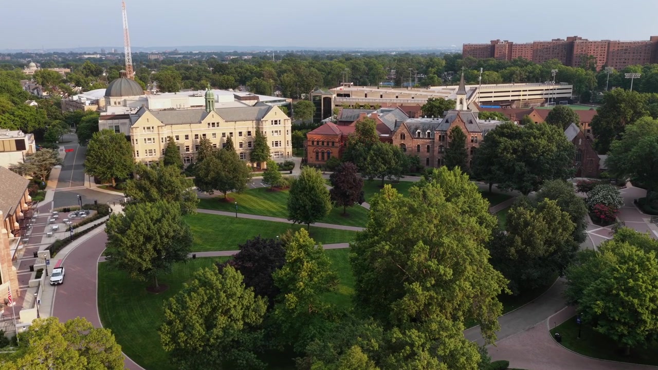Seton Hall -yliopiston kampusalue South Orangessa, New Jerseyssä esittelee historiallisia tiilirakennuksia, kupolikattoisen kellotornin ja hoidettuja nurmikoita tiheiden vihreiden kesäpuiden keskellä. Ilmakuva dronella.