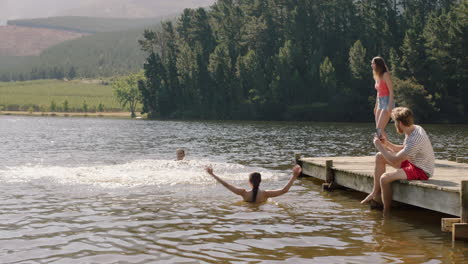 Junger-Mann-Schnappt-Sich-Eine-Frau,-Die-Mit-Ihr-In-Den-See-Springt-Und-Im-Wasser-Planscht.-Eine-Gruppe-Von-Freunden-Hängt-An-Einem-Sommernachmittag-Herum-Und-Genießt-Den-Urlaub