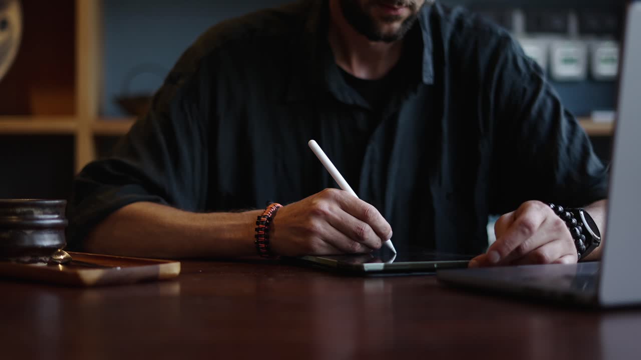 A man using a stylus on a tablet at a desk, possibly creating digital art or designs