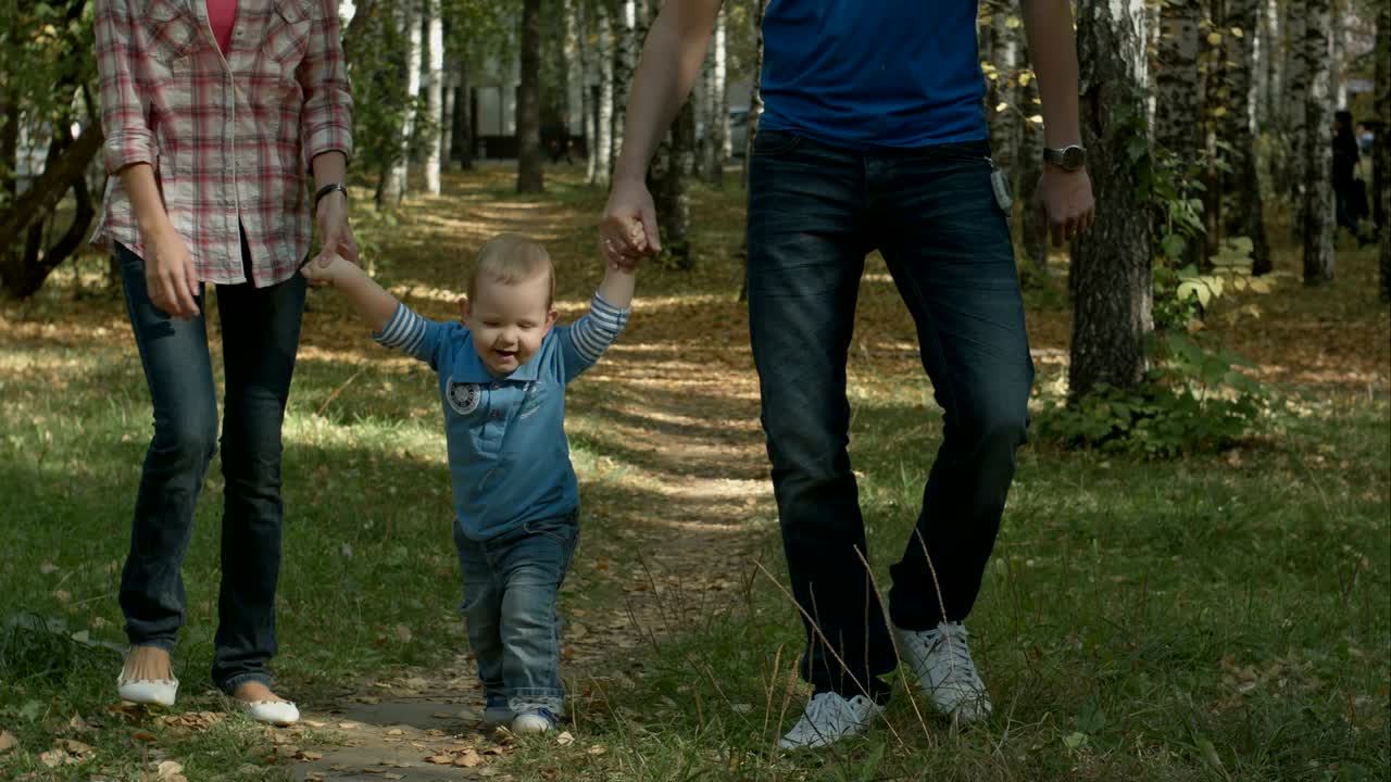 una feliz familia joven se está divirtiendo en el parque de otoño al aire libre en un día soleado. madre, padre y su pequeño bebé corren en el par