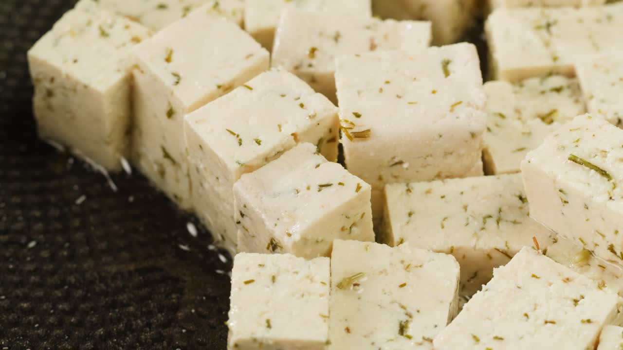 Fried tofu with sesame seeds and spices on cast iron pan, cooking japanese salad. Healthy ingredient for cooking vegan vegetarian diet food. Roasted tofu over black background.