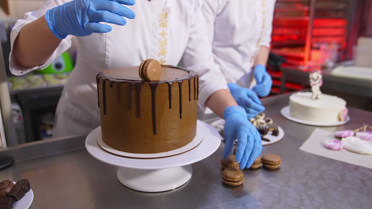Big beautiful chocolate cake decoration in the confectionary. Pastry cook puts the macaroons on cake top. Close up.