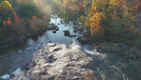 rocky river with fall woods on the sides and the sunlight right up front