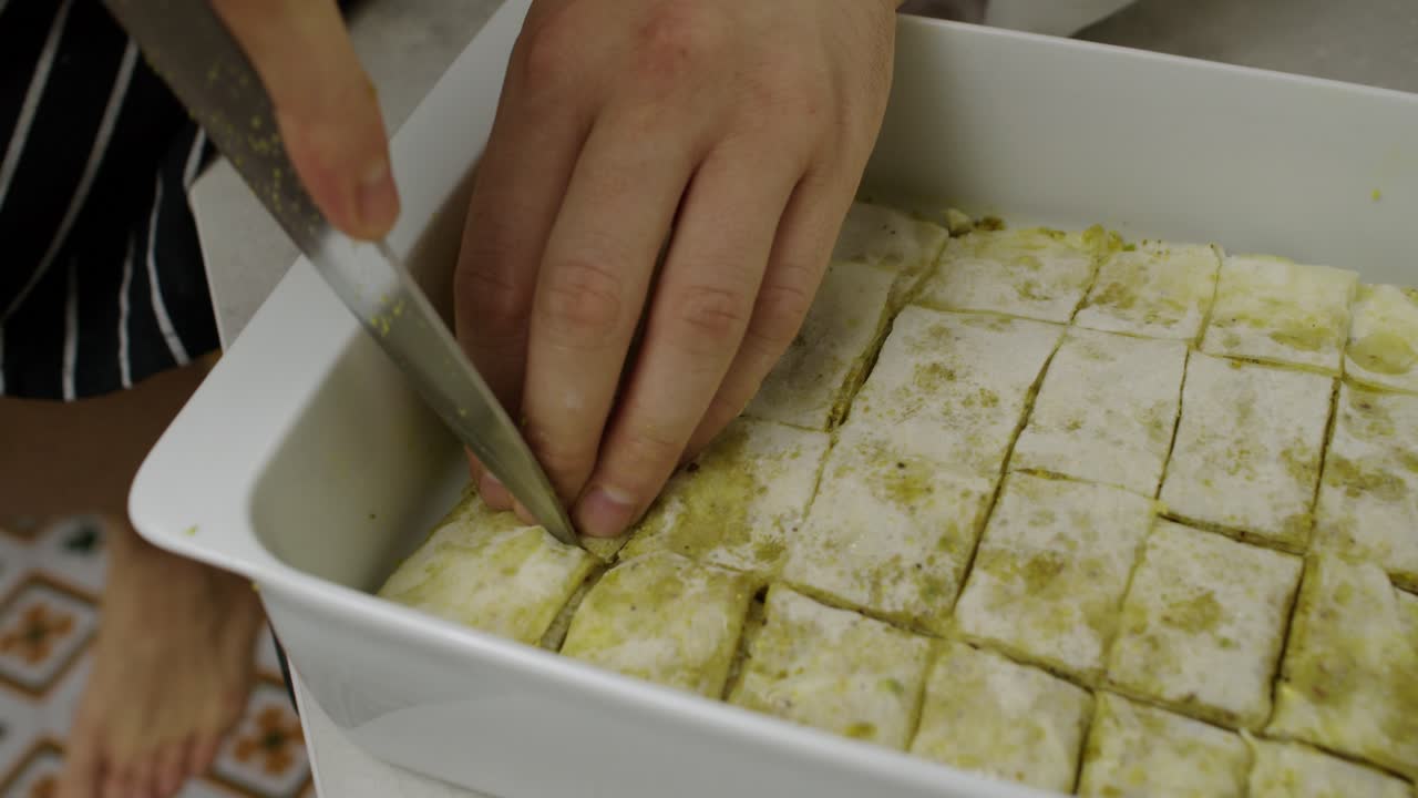 el chef corta el baklava árabe en rodajas dentro de la bandeja de cocción de cerámica