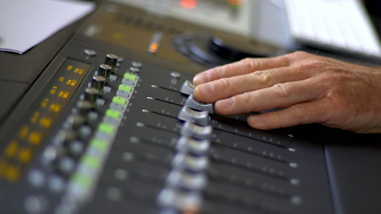 manos moviendo faders en una mesa de mezclas de audio en un estudio de grabación