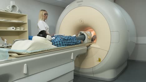 woman doctor makes knee-joint mri scanning. young man patient on automatic table leaves a closed-type mri machine using noise isolation headphones. modern equipment, coil on the patient's knee