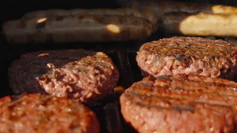 close up of meat free burgers being flame grilled on bbq in evening light with plant based sausages in background