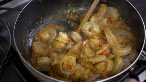 plato de camarones con curry agitado por un cucharón de madera mientras se cocina dentro de la sartén