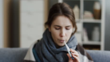 Close-Up-Of-The-Young-Ill-Woman-In-The-Warm-Scarf-And-A-Plaid-Measuring-A-Temperature-And-Showing-Thermometer-As-She-Having-An-Influenza