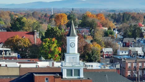 a white clock tower stands tall amid autumn-colored trees in a serene town