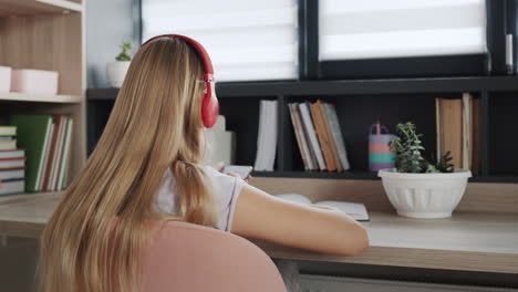 la niña está ocupada con una computadora portátil en su habitación, al lado de ella hay un gato rojo