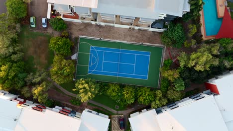 aerial shot of a tennis court surrounded by trees in a residential area, showcasing outdoor amenities