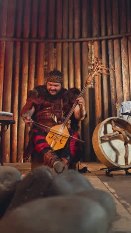 folk rock band plays traditional altai music with ancient instruments near stone statue in ail house. emotional integration of old culture in modern life
