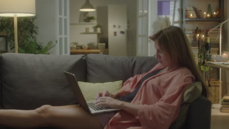 woman typing on laptop of sofa at home