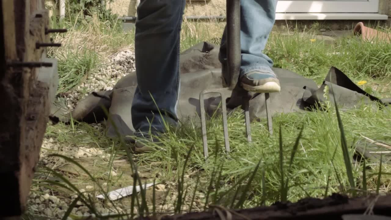 창고 문을 통해 포크 pov로 정원에서 흙을 돌리는 정원사