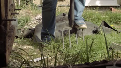 gardener turning soil in garden with fork pov through shed door