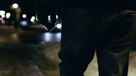 Follow-shot-of-a-hooded-man-walking-down-a-cold-winter-street-before-tilting-down-to-his-feet-in-slow-motion