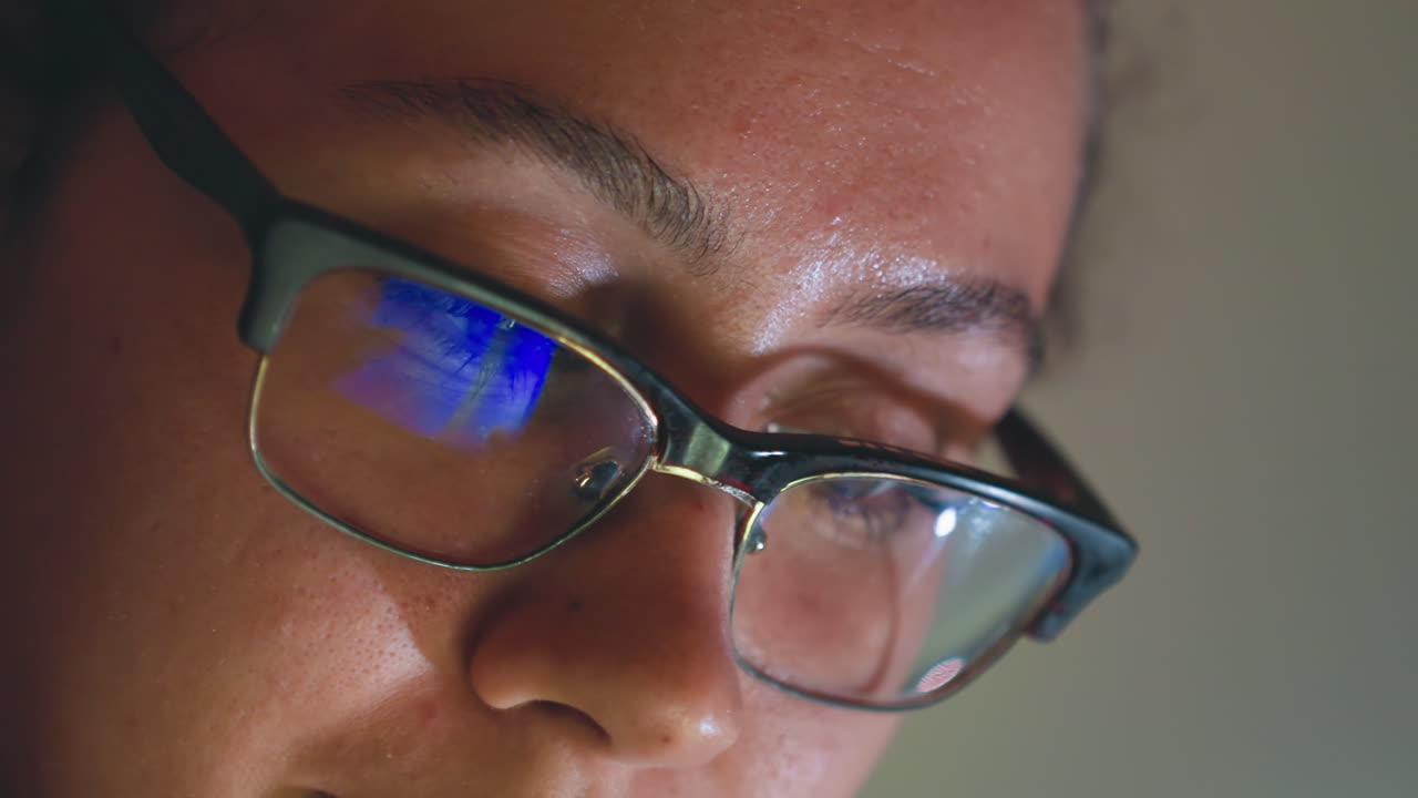 Primo piano di una donna con occhiali che programma a tarda notte, vivido riflesso blu dello schermo nelle lenti, espressione concentrata con goccioline di sudore, digitazione sulla tastiera e debug rapido, urgenza da startup e scadenza imminente.