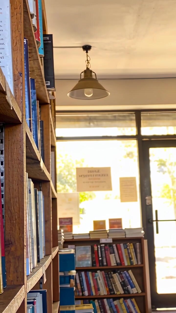 Vertical video: Reaching woman in white tee pulling paperback, exiting bookshop via door