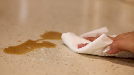 a hand wipes a coffee spill on a countertop using a cloth, under warm lighting