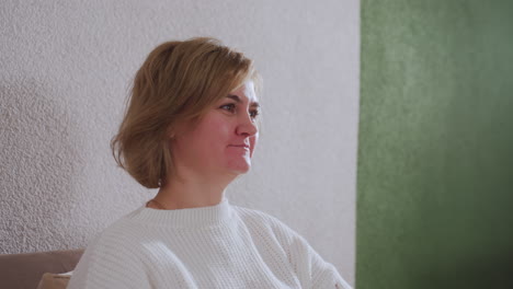 gentle guest smiles warmly during therapy session on sofa engaging with counselor in cozy interior with soft curtains table evening light creating calm atmosphere highlighting empathic exchange
