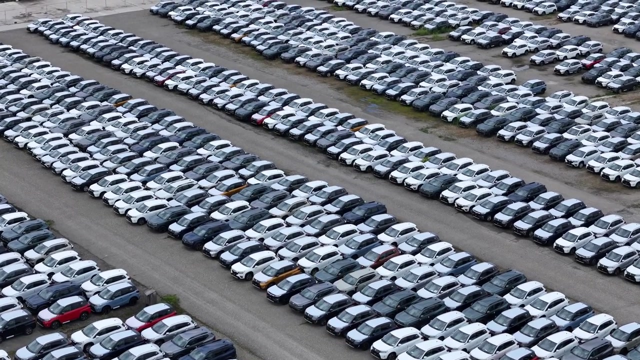Yüzlerce yeni binek araç, sıkıca düzenlenmiş sıralar halinde geniş bir araç depolama ve dağıtım alanını dolduruyor, otomotiv lojistiği ve envanterini vurguluyor, drone ile havadan çekim.
