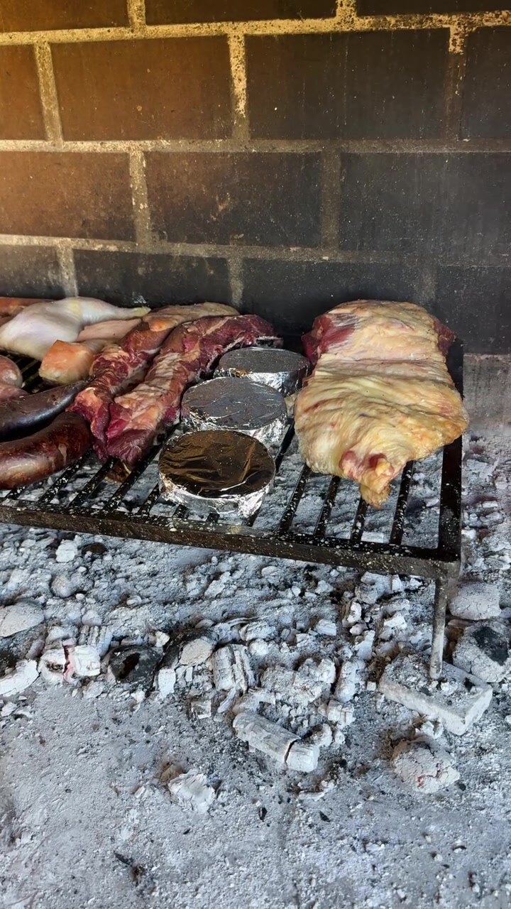 Asado tradisional Argentina dengan daging sapi, sosis darah, sosis, ayam, dan sayuran yang dimasak di atas bara kayu panas di dalam perapian terbuka, close-up panning vertikal.