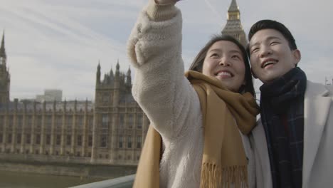 joven pareja asiática de vacaciones posando para selfie frente a las casas del parlamento en londres, reino unido 1