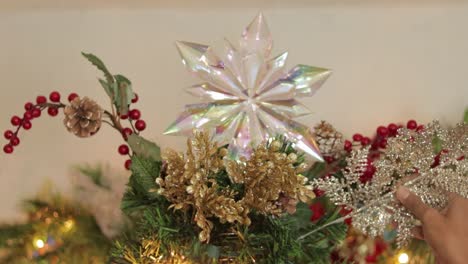 placing silver sprig on decorated top of christmas tree with star