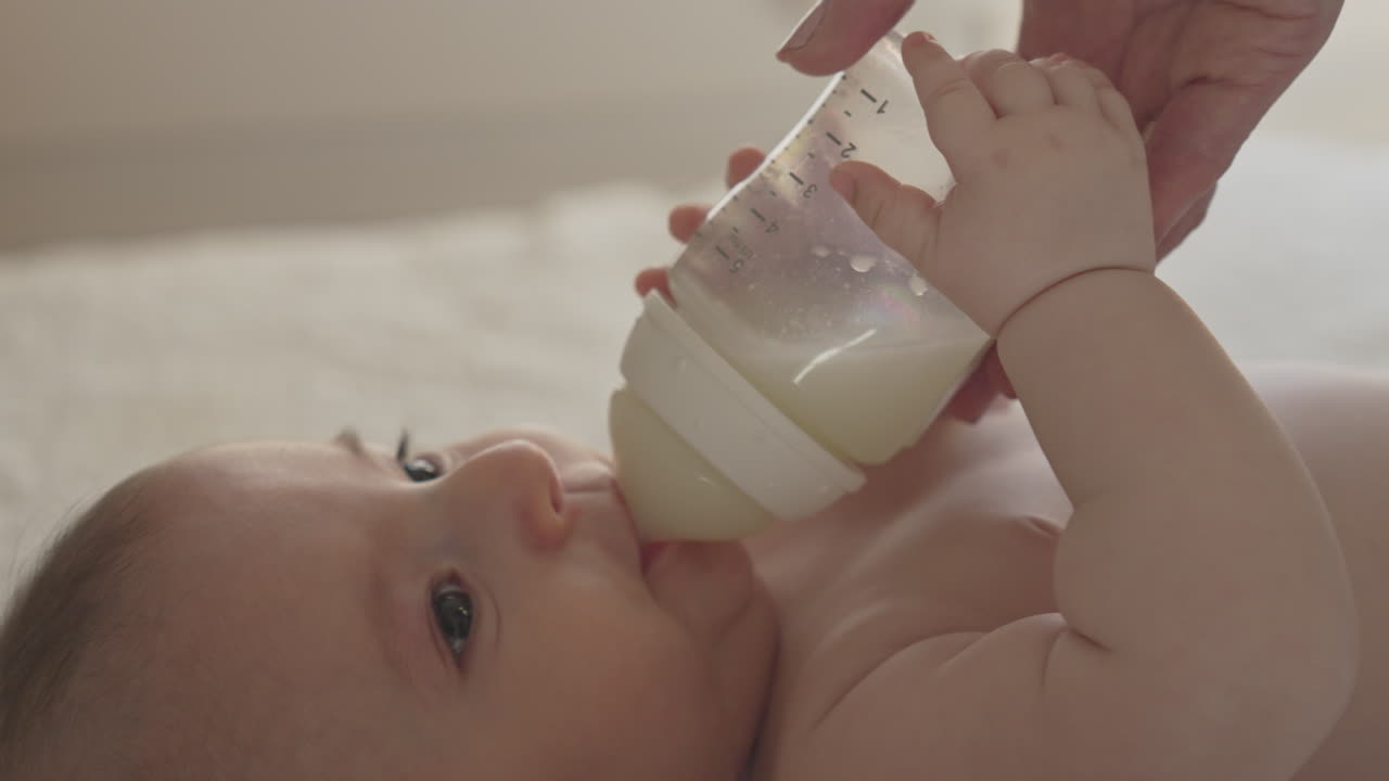 primer plano recién nacido alimentándose con biberón sostenido por las manos de la madre, bebé chupando leche