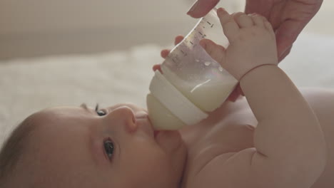 closeup newborn feeding on bottle held by mother's hands, baby sucking on milk