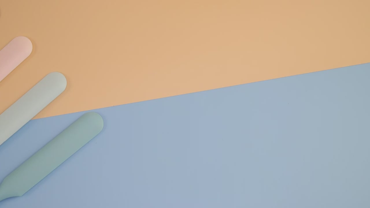 Four pastel silicone spatulas are neatly arranged on a soft-toned peach and blue background in a minimalist flat lay style.