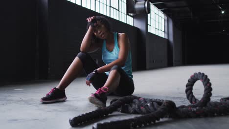 mujer afroamericana descansando después de luchar con cuerdas en un edificio urbano vacío