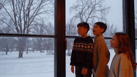 children gazing at a snowy winter scene from a window