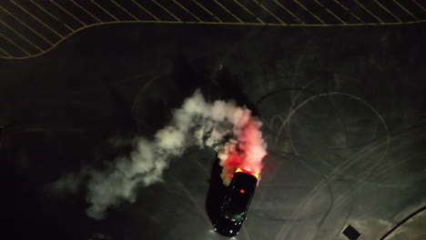 aerial view above a car burning tires at a nighttime parking lot - cenital, drone shot