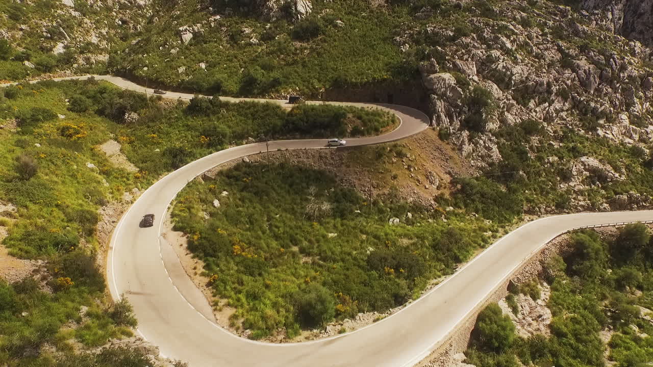 Vista aerea dal basso che avanza lungo una strada di montagna tortuosa mentre le auto salgono attraverso un terreno roccioso e verde a Maiorca
