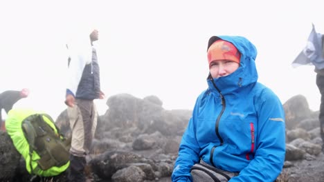a tourist rests on a stone in the mountains during rain and fog