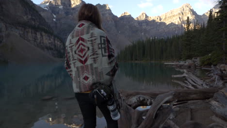 Girl-walking-on-a-tree-trunk,-sun-rising-on-Moraine-Lake-on-the-back