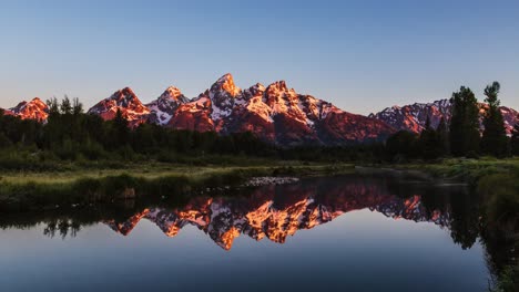 Amazing-golden-sunrise-time-lapse,-light-hitting-snow-capped-mountain-with-mirror-lake-reflection-at-Schwabachers-Landing,-Grand-Teton-National-Park,-Wyoming-United-States