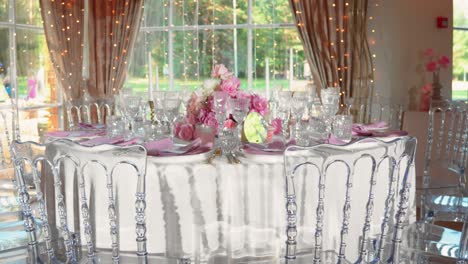 shot of fancy wedding reception table with glasses and plates, table is decorated with gorgeous pink and white roses and white candles, zoom in shot