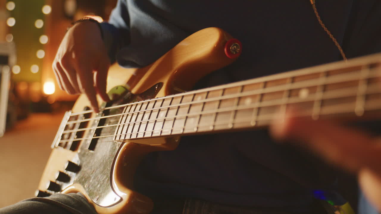 Primo piano statico di una mano che pizzica le corde di un basso in un caldo studio con luci bokeh